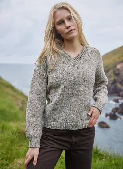 blonde woman standing in front of irish cliffs wearing a grey knit wool sweater